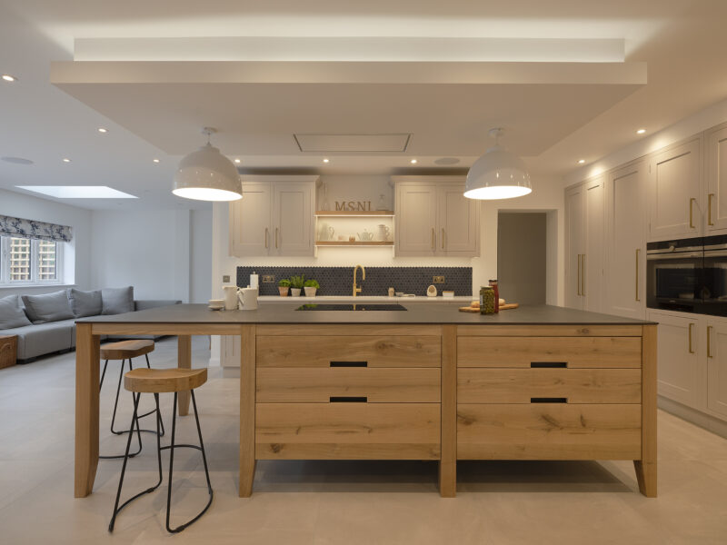 Light oak island with dark grey quartz worktop, metal pendant lights and bar stools in an open-plan kitchen